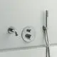 Chromfarbener Badethermostat mit Handbrause und Wasserhahn von Ideal Standard, montiert an einer hellen Wand. Bedienungselemente sichtbar, funktionale Gestaltung.